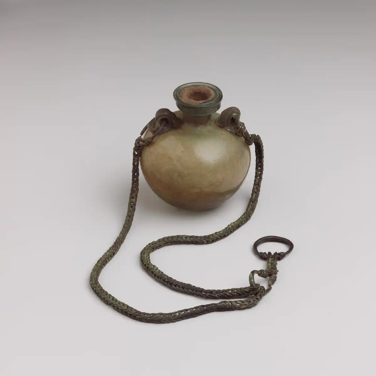 Pale green Roman glass flask with a rounded body and a braided bronze chain ending in a carrying ring.
