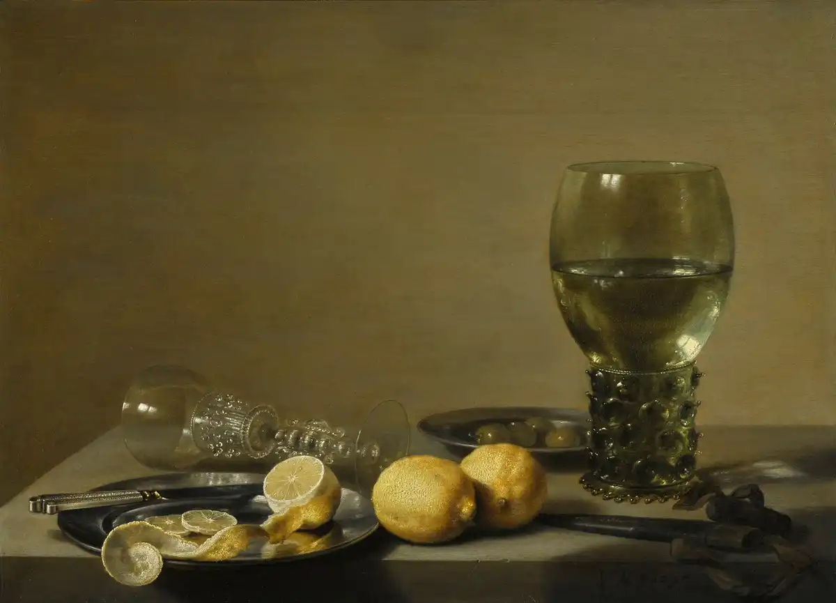 Dutch still life of two lemons, one half-peeled with its rind spiralling off the table edge, beside a dish of green olives, a knife and tall glasses.