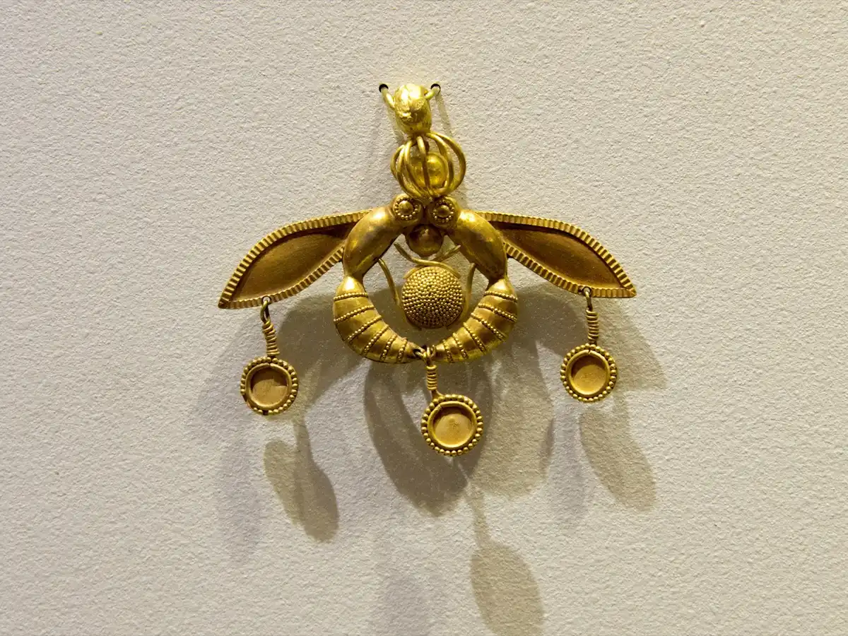 Minoan gold pendant of two bees curved around a granulated disc, holding it between them.
