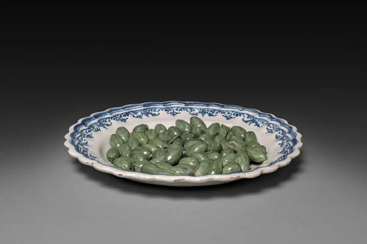 Faience plate on which dozens of small green ceramic olives are modelled in relief, as if heaped for the table.