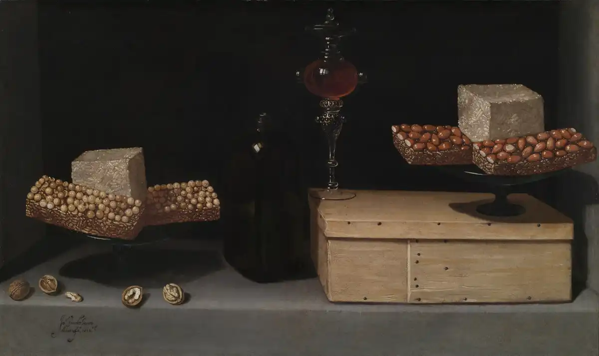 Spanish still life of pale blocks of nut-and-honey turrón on a fluted stand and wrapped in paper, with a wooden box and small sweets on a stone ledge.
