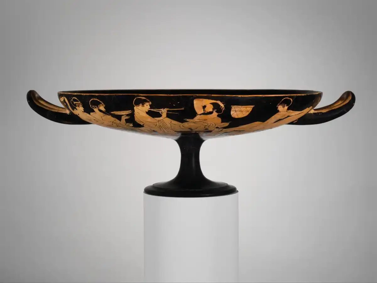 Exterior of an Attic red-figure kylix showing reclining symposiasts with drinking cups and an aulos player.